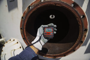 Worker hand holding gas detector inspection safety gas testing at front manhole tank to work inside confined