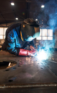 Professional industrial welder welding metal parts in metalworking factory.